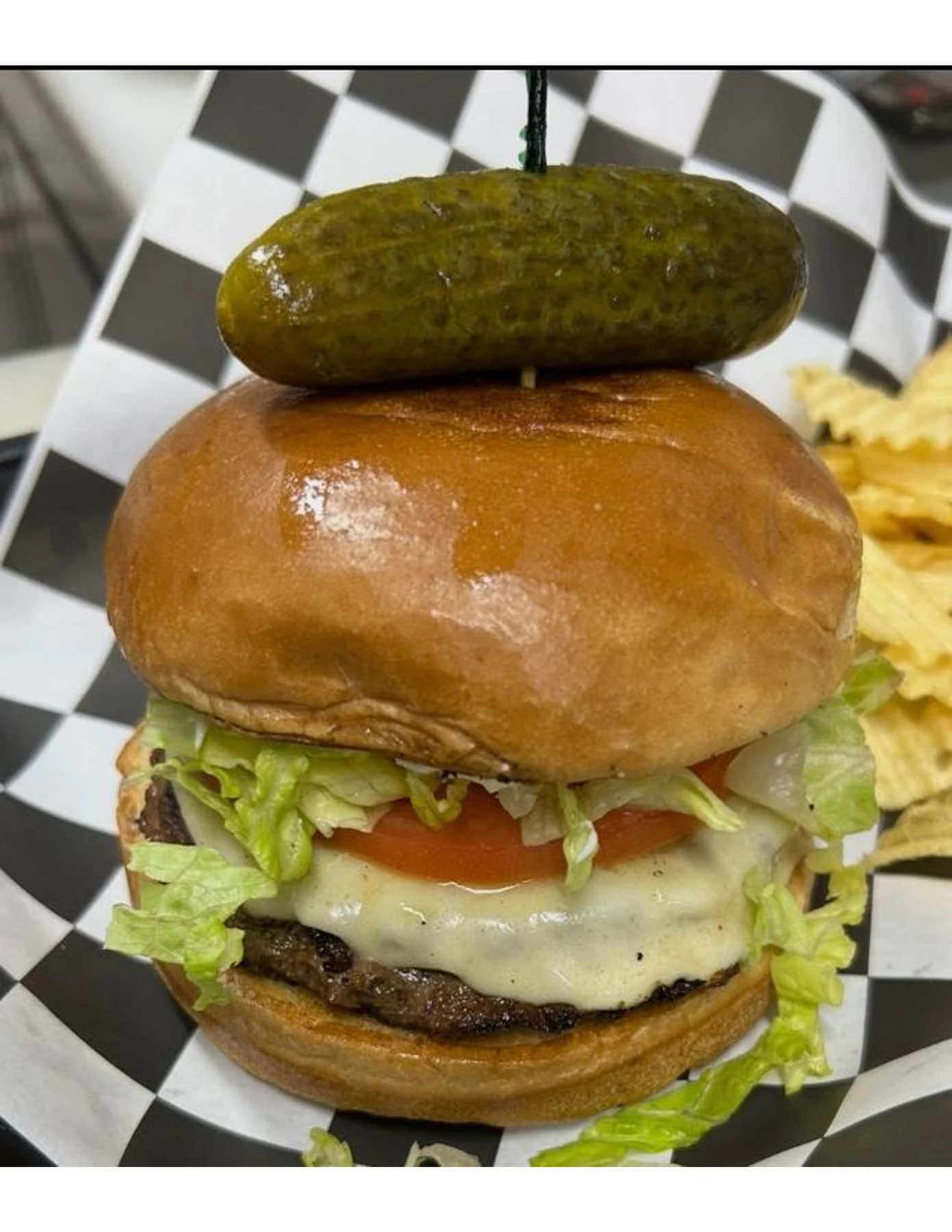 Burger with melted cheese, lettuce, tomato, and a pickle at Dewberry Kitchen & Tap